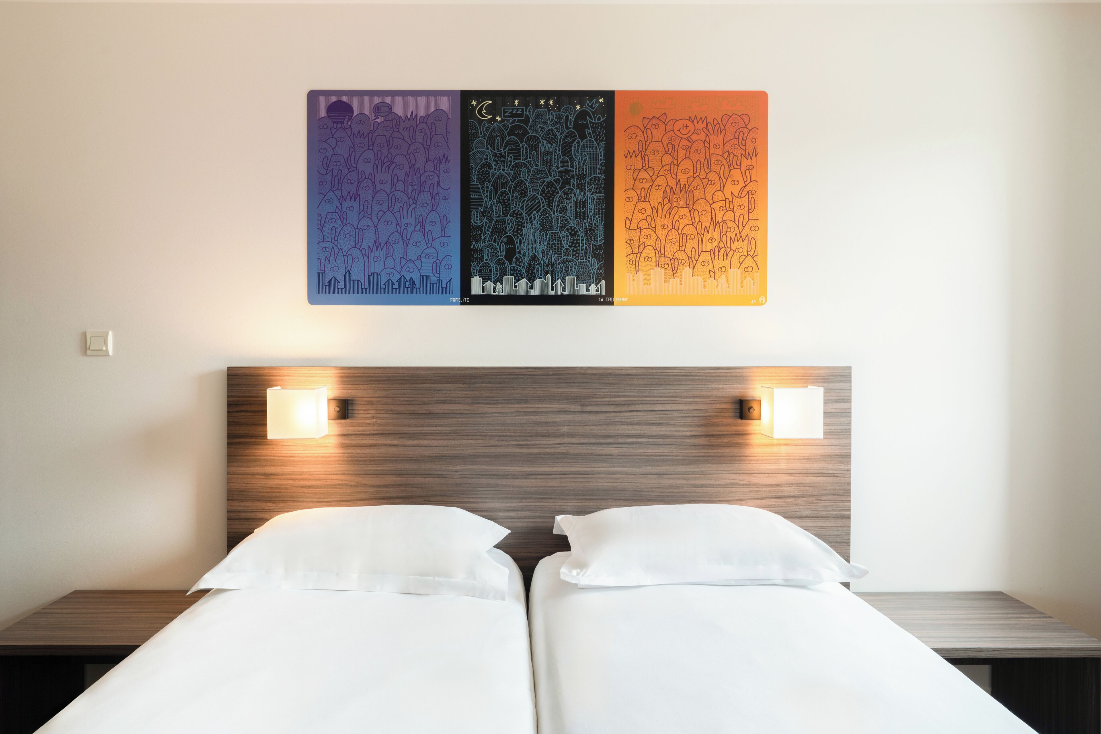 A hotel room with two beds, a wooden headboard, wall-mounted lights, and a colorful artwork above the beds.