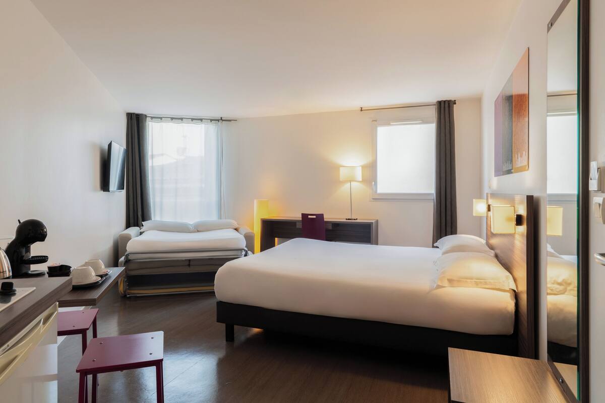 A hotel room with a bed, bedside tables, a desk with a chair, a lamp, and a TV mounted on the wall.