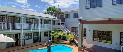A two-story building with a swimming pool, outdoor seating, and a covered patio area.
