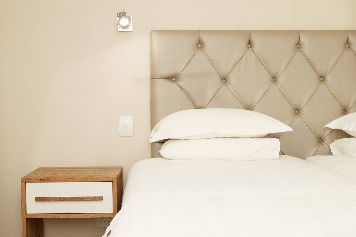 A bedroom with a tufted headboard, a wooden nightstand with a drawer, and white bedding.