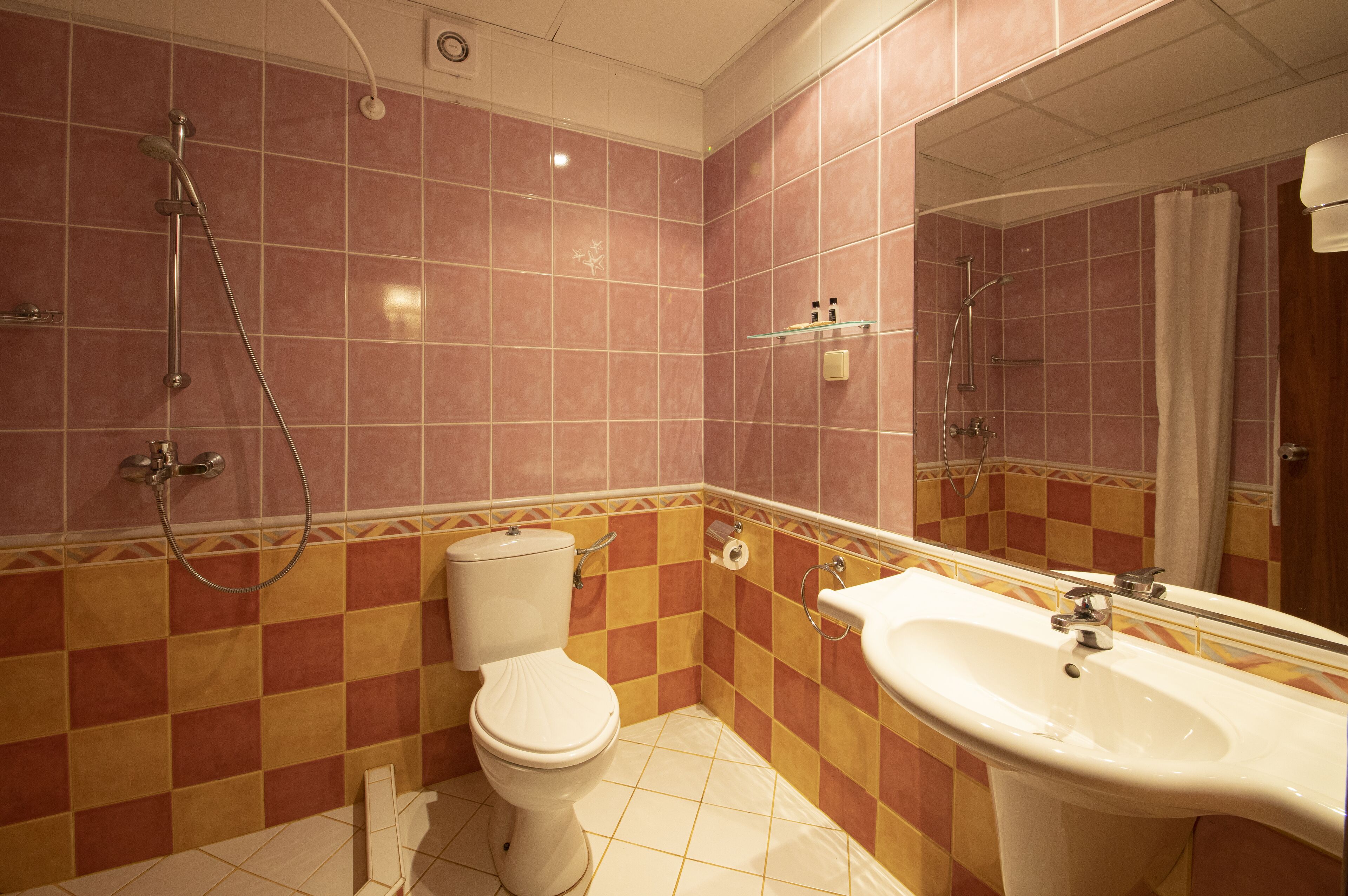 A bathroom with pink and yellow checkered tiles, a white toilet, a sink, and a shower.