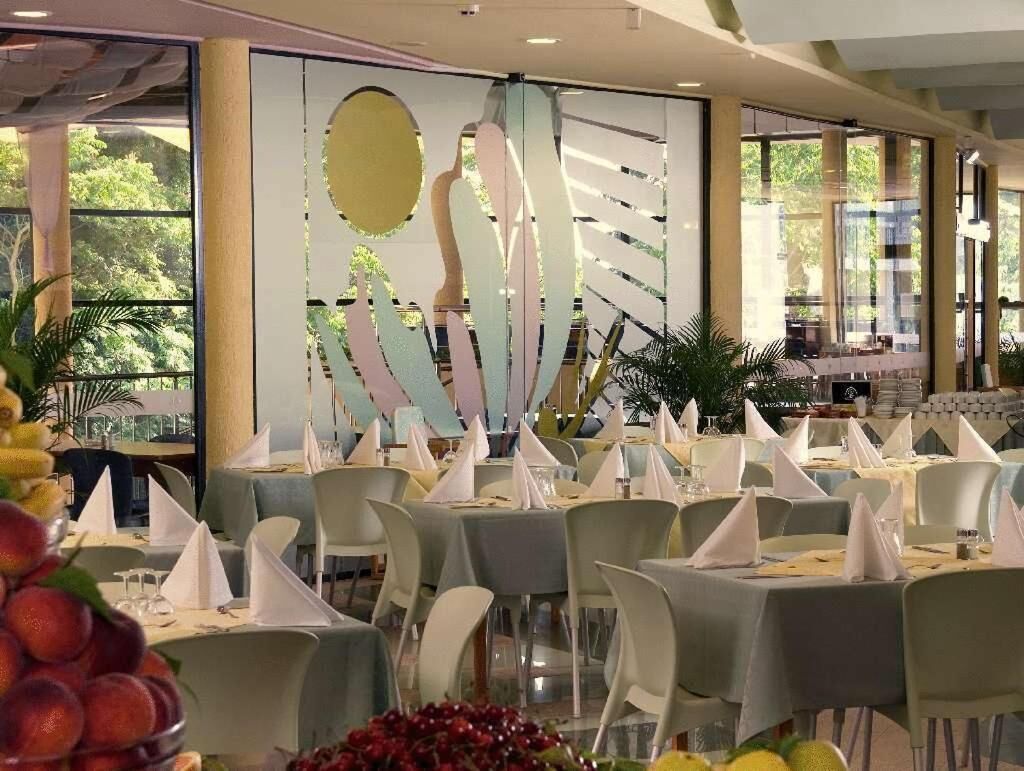 A restaurant with round tables, white chairs, and a decorative wall with abstract art.
