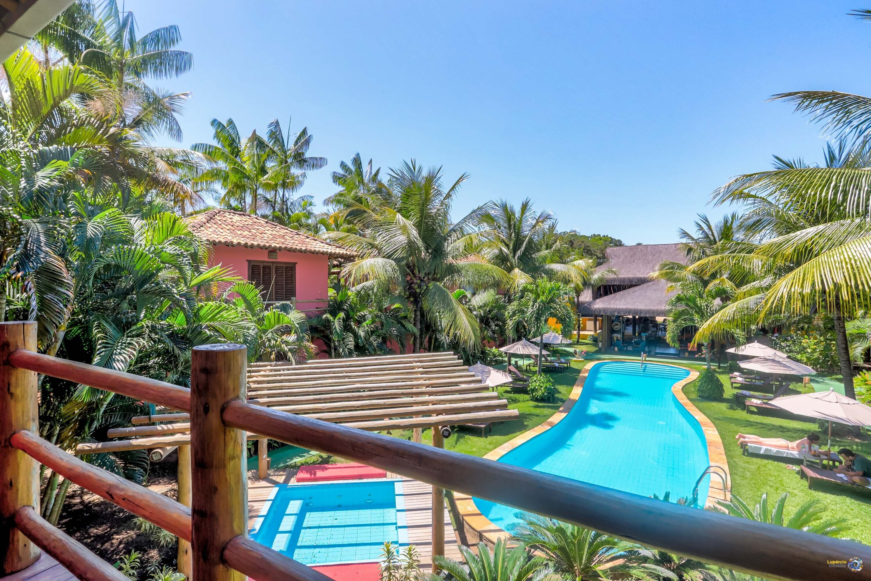 A pool area with a wooden deck, palm trees, and a building with a red roof.