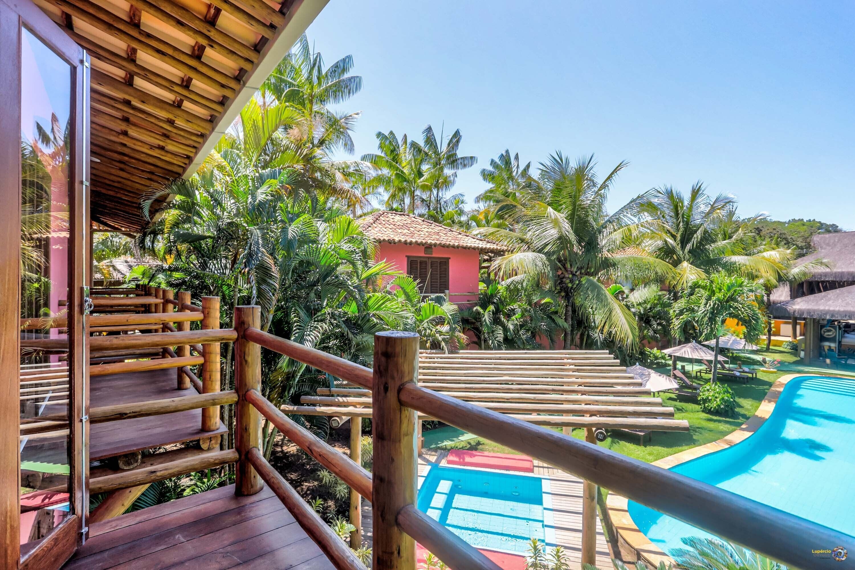 A wooden deck with a pool, surrounded by palm trees and a small building.