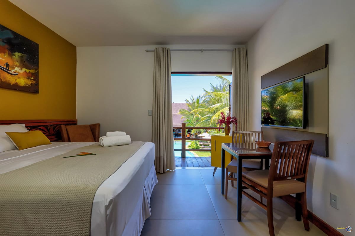 Camera d'albergo con un letto, una scrivania, una sedia, una TV e un balcone con vista sulle palme.