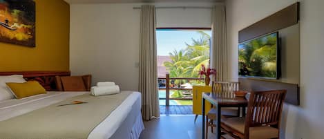 Habitación de hotel con cama, escritorio, silla, televisor y balcón con vistas a palmeras.