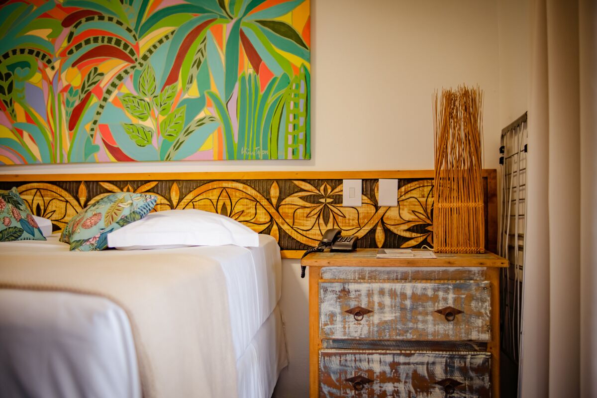 A hotel room with a bed, a wooden nightstand, a telephone, and a colorful abstract painting on the wall.