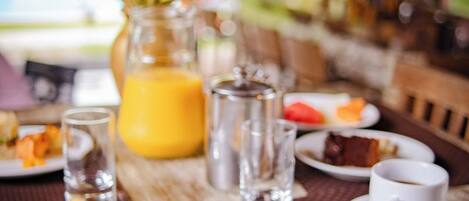 A dining table with breakfast items, a glass of orange juice, and a vase with flowers.