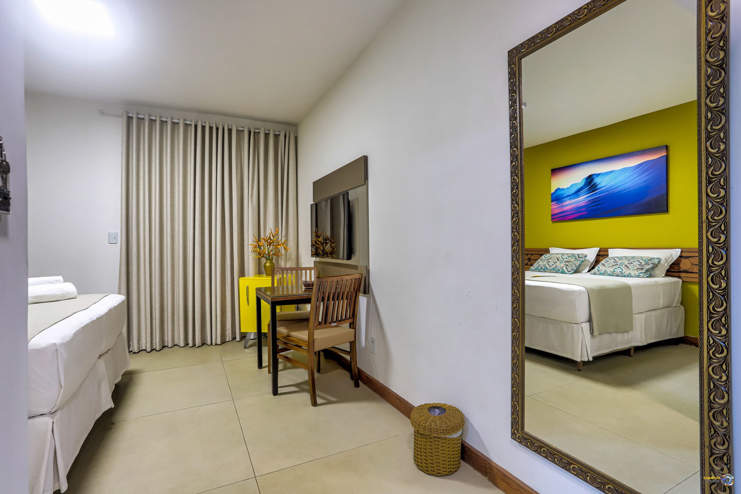 Una habitación de hotel con cama, escritorio con silla, televisión y un espejo grande que refleja el espacio.