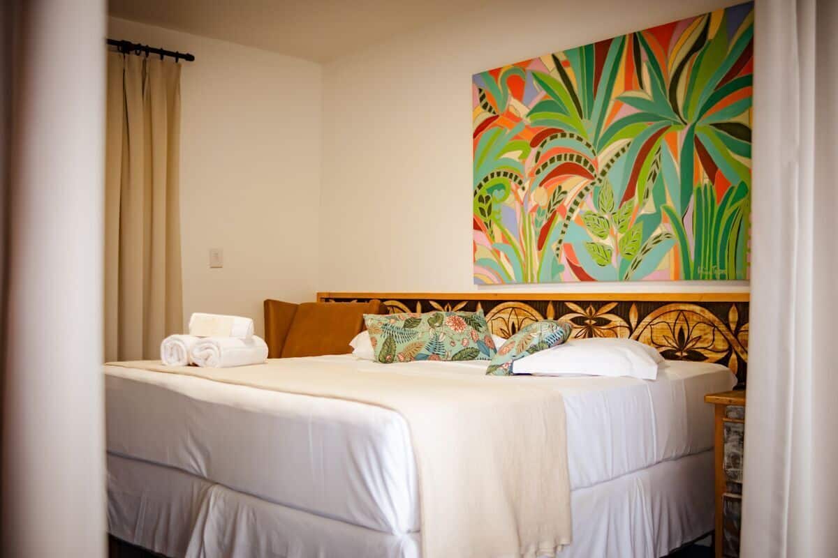 Una camera d'albergo con un letto, una testiera con motivo floreale, un quadro colorato e una tenda.
