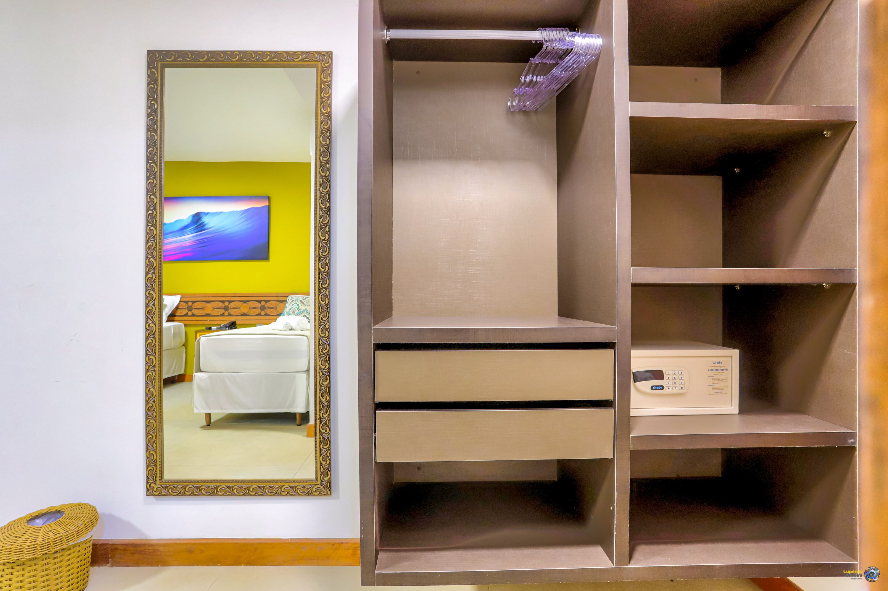 Une pièce avec un grand miroir, un lit, une armoire avec des étagères et une petite table sur laquelle se trouve un appareil.