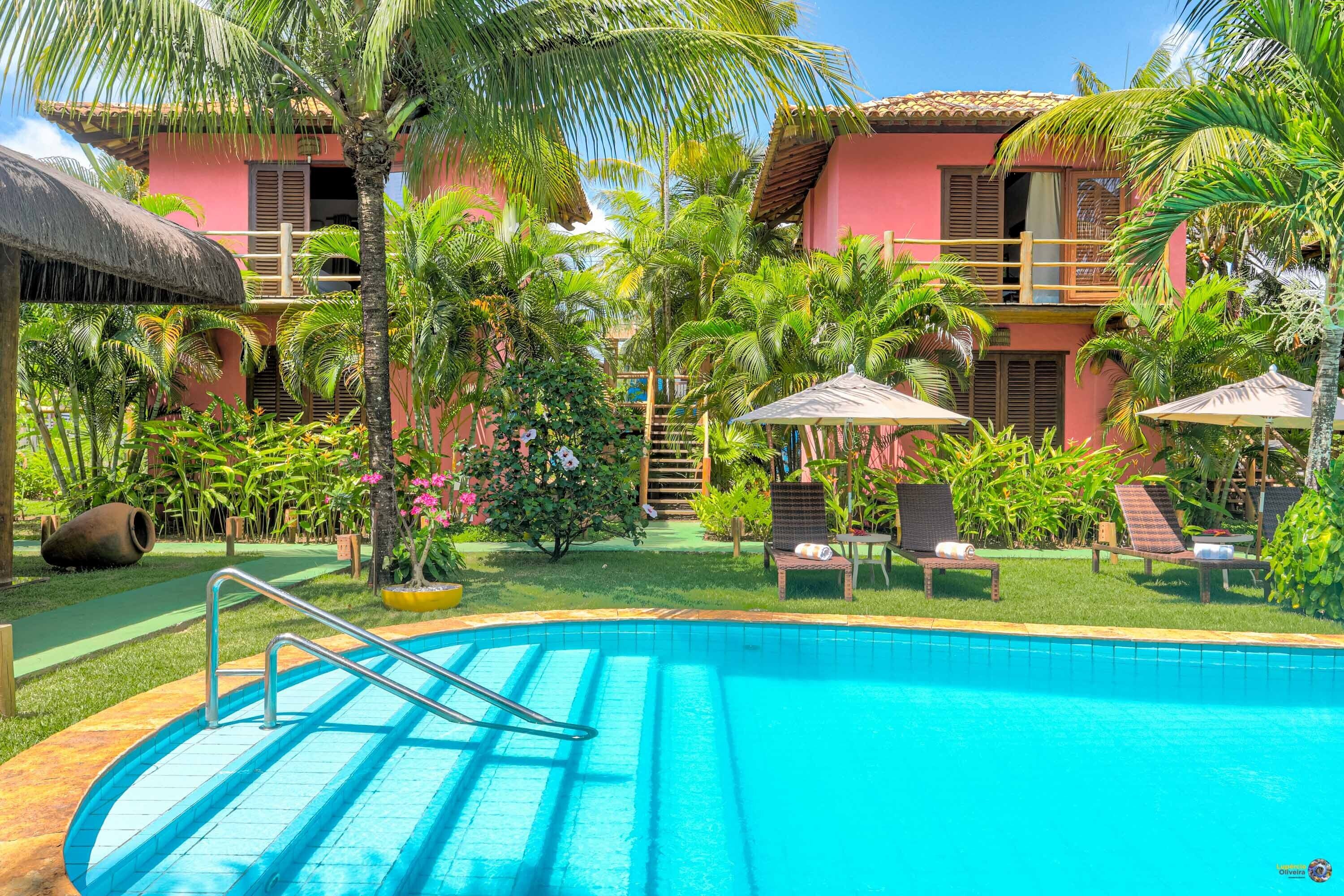 A swimming pool with a metal ladder, surrounded by lush greenery and palm trees.