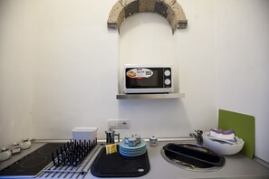 A kitchen with a microwave, a kettle, a sink, and a green cutting board.