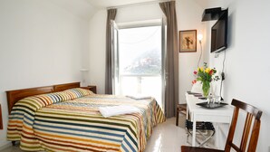 A hotel room with a bed, a desk with a chair, a television, and a window with curtains. - La Casa di Carla (Ravello)