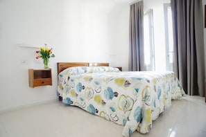 A bedroom with a bed, a nightstand, a vase with flowers, and a window with curtains.