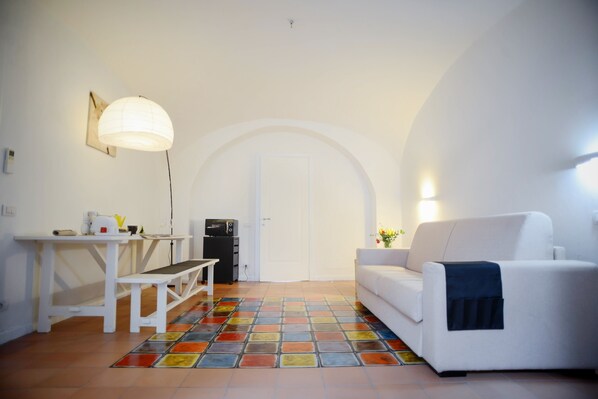 A modern living room with a white sofa, a bench, a table with a lamp, and a colorful tiled floor.