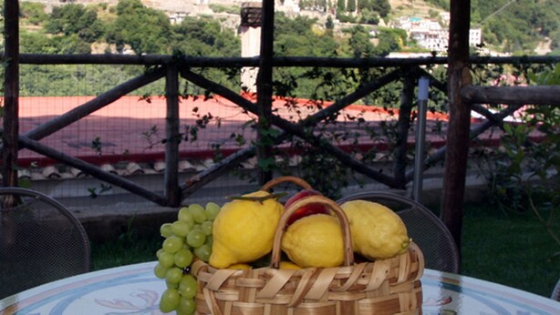 A wicker basket with lemons and grapes on a table with a floral pattern, overlooking a hillside with buildings. - La Casa di Carla (Ravello)