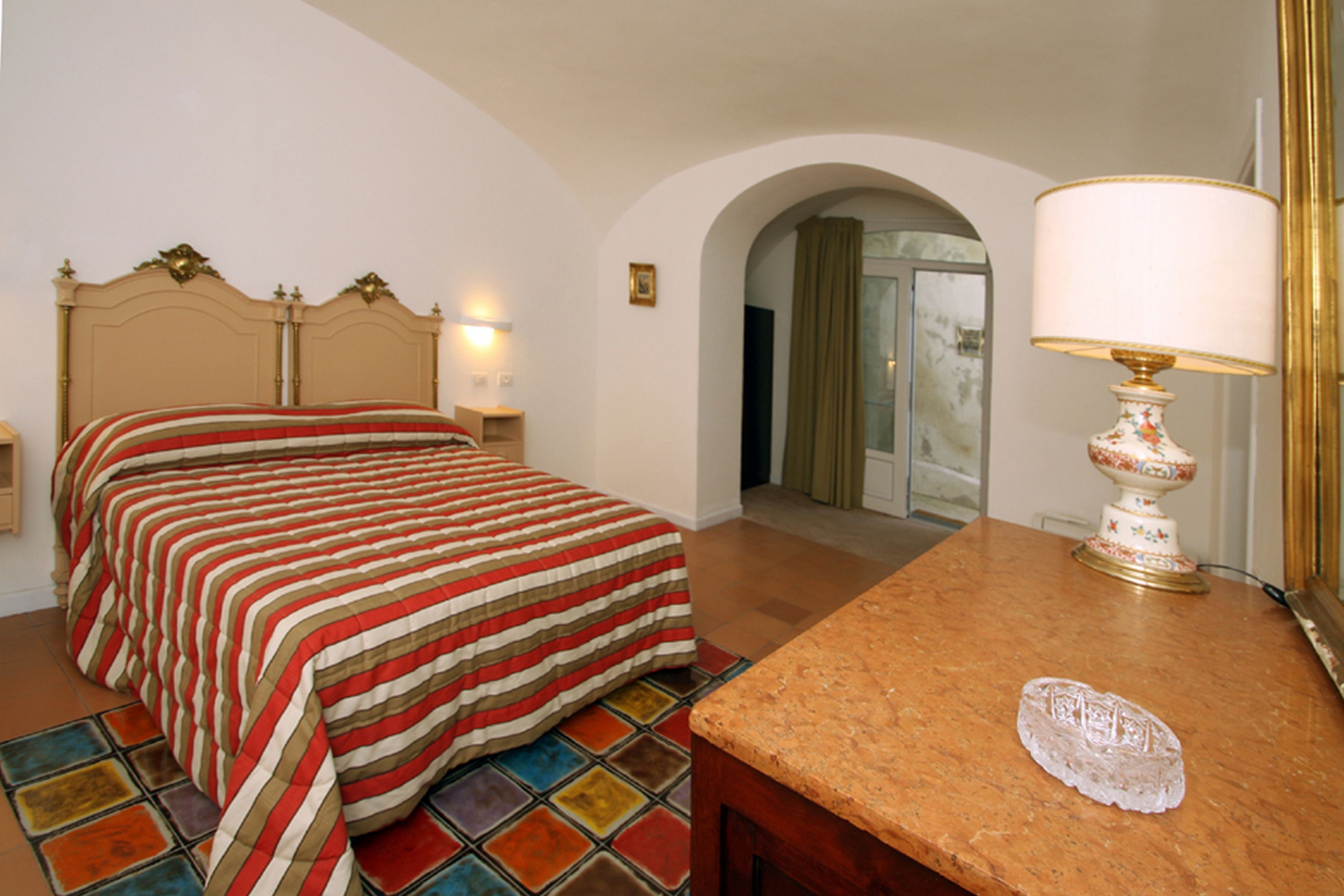 Une chambre d’hôtel avec un lit, une table de chevet, une lampe et un sol carrelé.