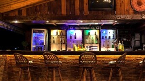 Un área de bar con interior de madera, taburetes de mimbre y estantes llenos de botellas.