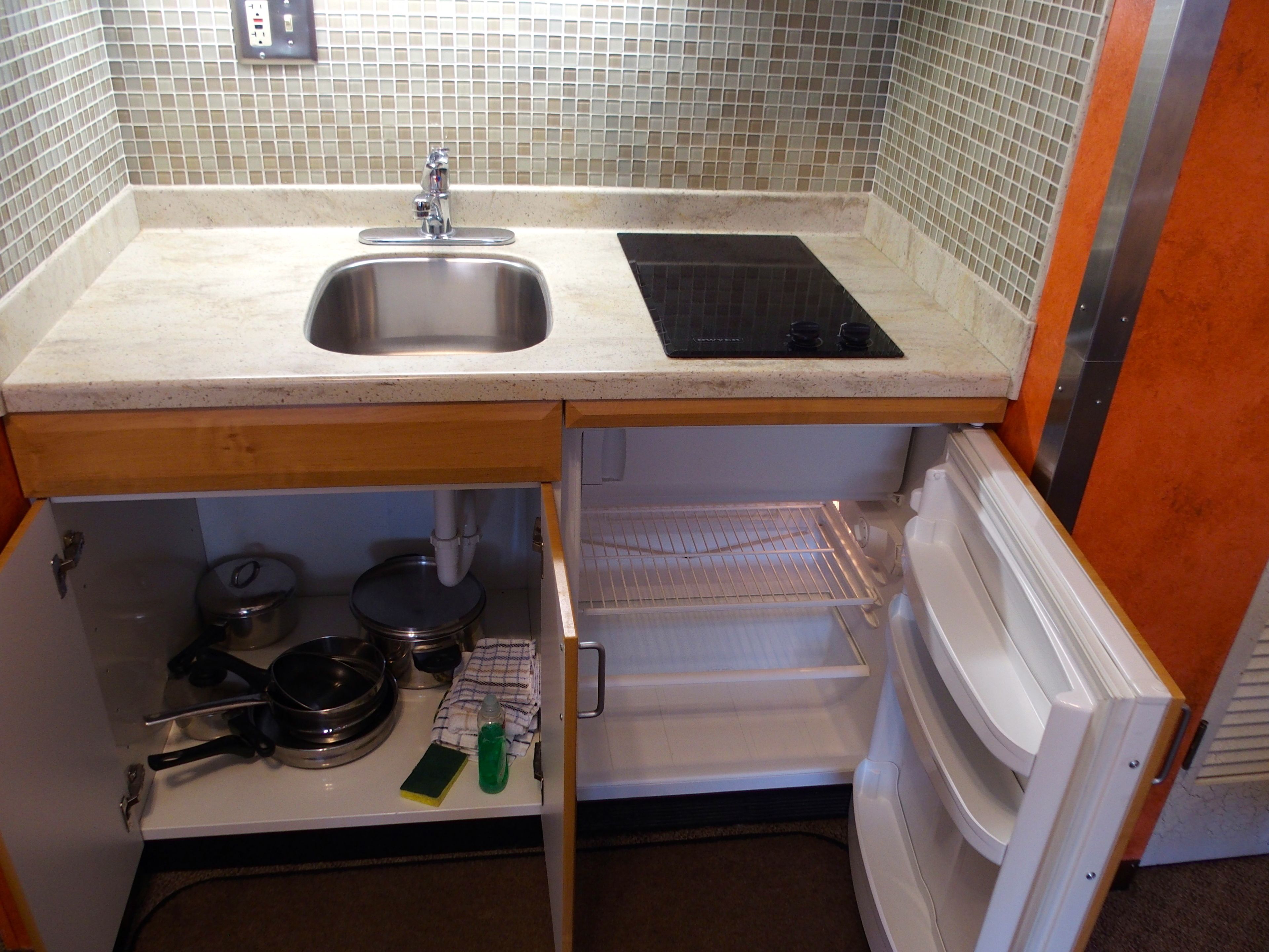 Cocina compacta con pileta de acero inoxidable, estufa eléctrica negra y refrigerador integrado.