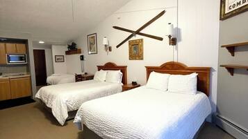 A hotel room with two beds, a ceiling fan, a kitchenette, and a painting on the wall.
