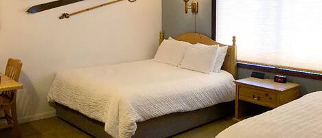 A hotel room with a bed, a nightstand with a lamp, a clock, and skis mounted on the wall.
