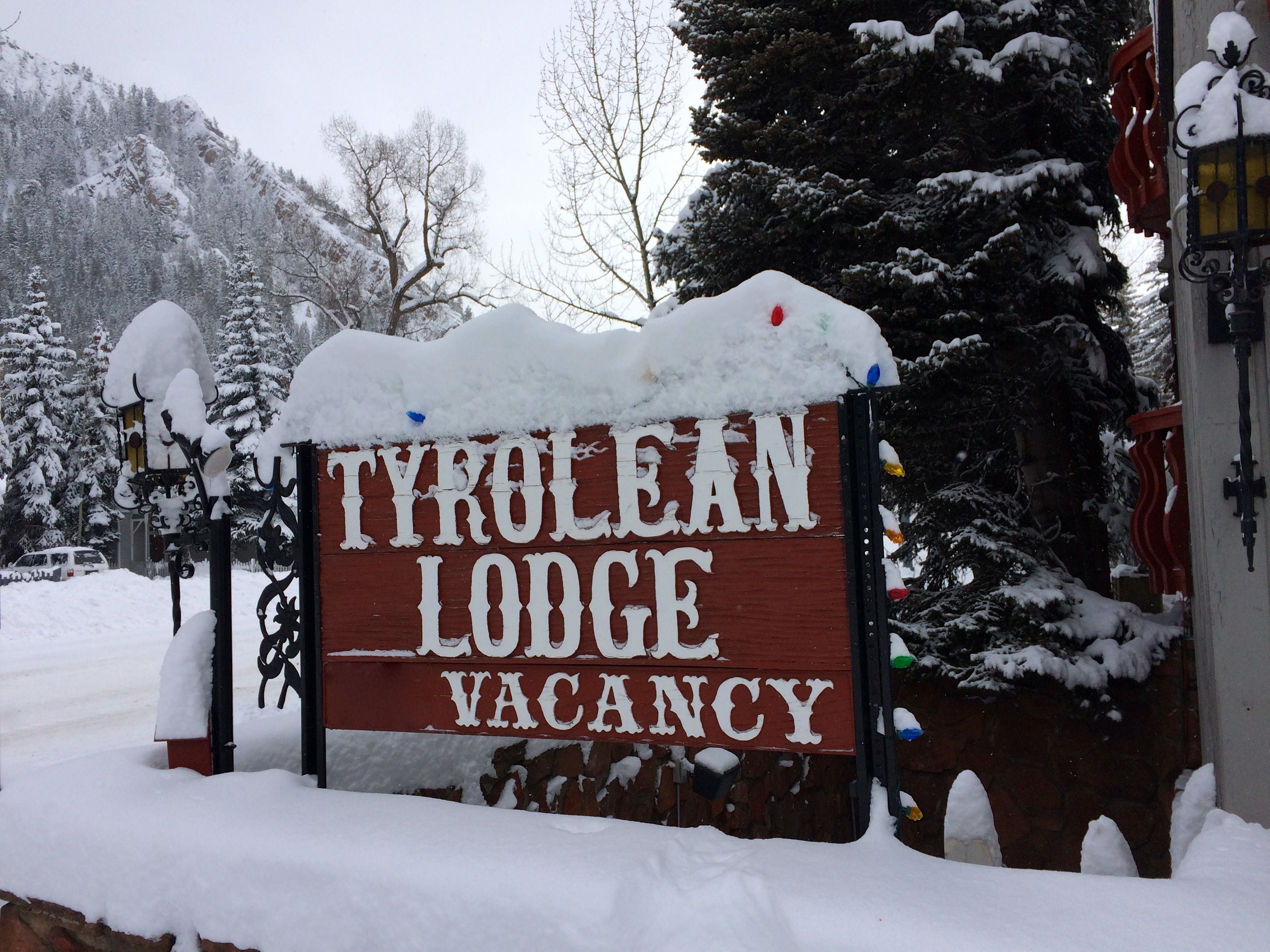 Ein hölzernes Schild mit der Aufschrift 'TYRULEAN LODGE VACANCY', teilweise von Schnee bedeckt.