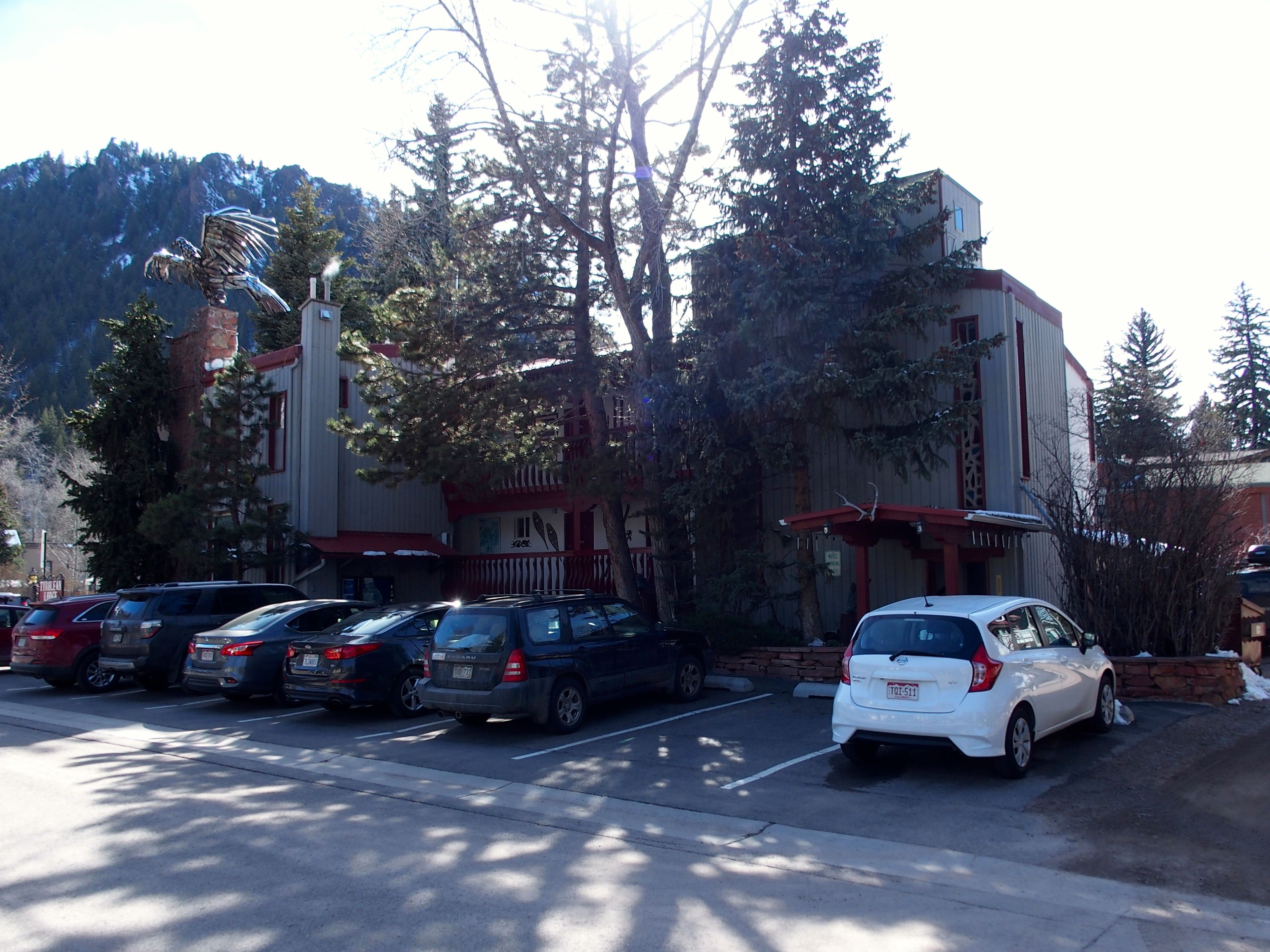 A parking lot with several cars, a building with a red and white facade, and trees in the background.