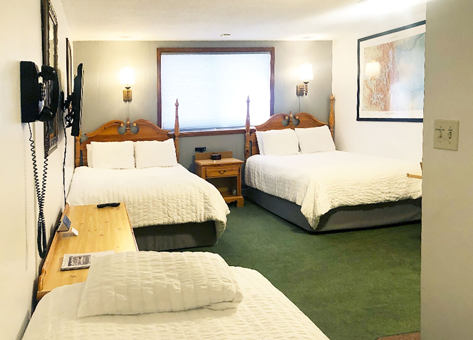 Une chambre d’hôtel avec deux lits simples, une table de chevet en bois, un bureau avec un téléphone et une fenêtre donnant sur un paysage agréable.