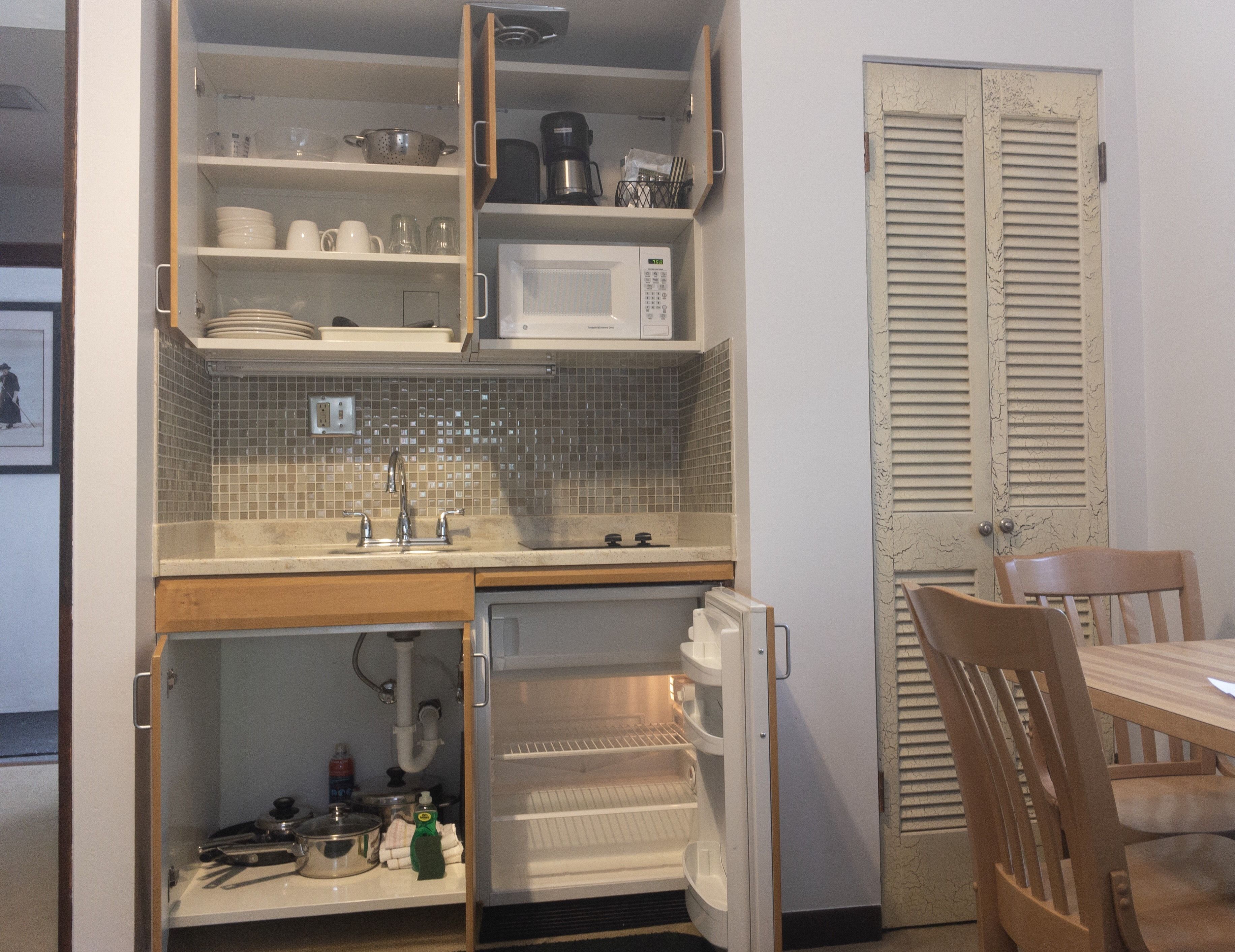 Cocina compacta con microondas, lavabo y nevera abierta.