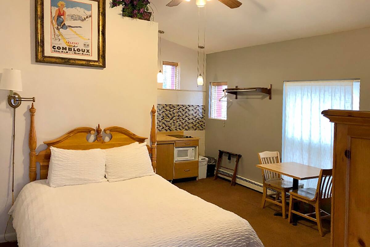 A bedroom with a bed, a desk, a chair, a microwave, and a ceiling fan.