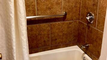 A bathroom with a bathtub, a handrail, and brown tiled walls.