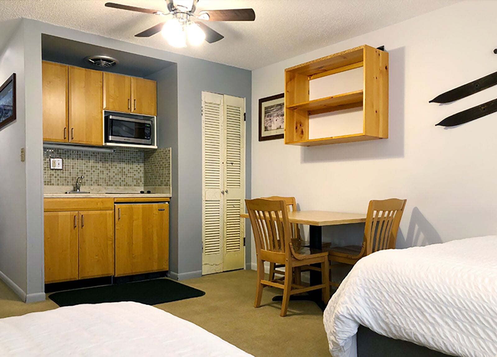 A compact room with a kitchenette, two wooden chairs, a small table, and a bed.