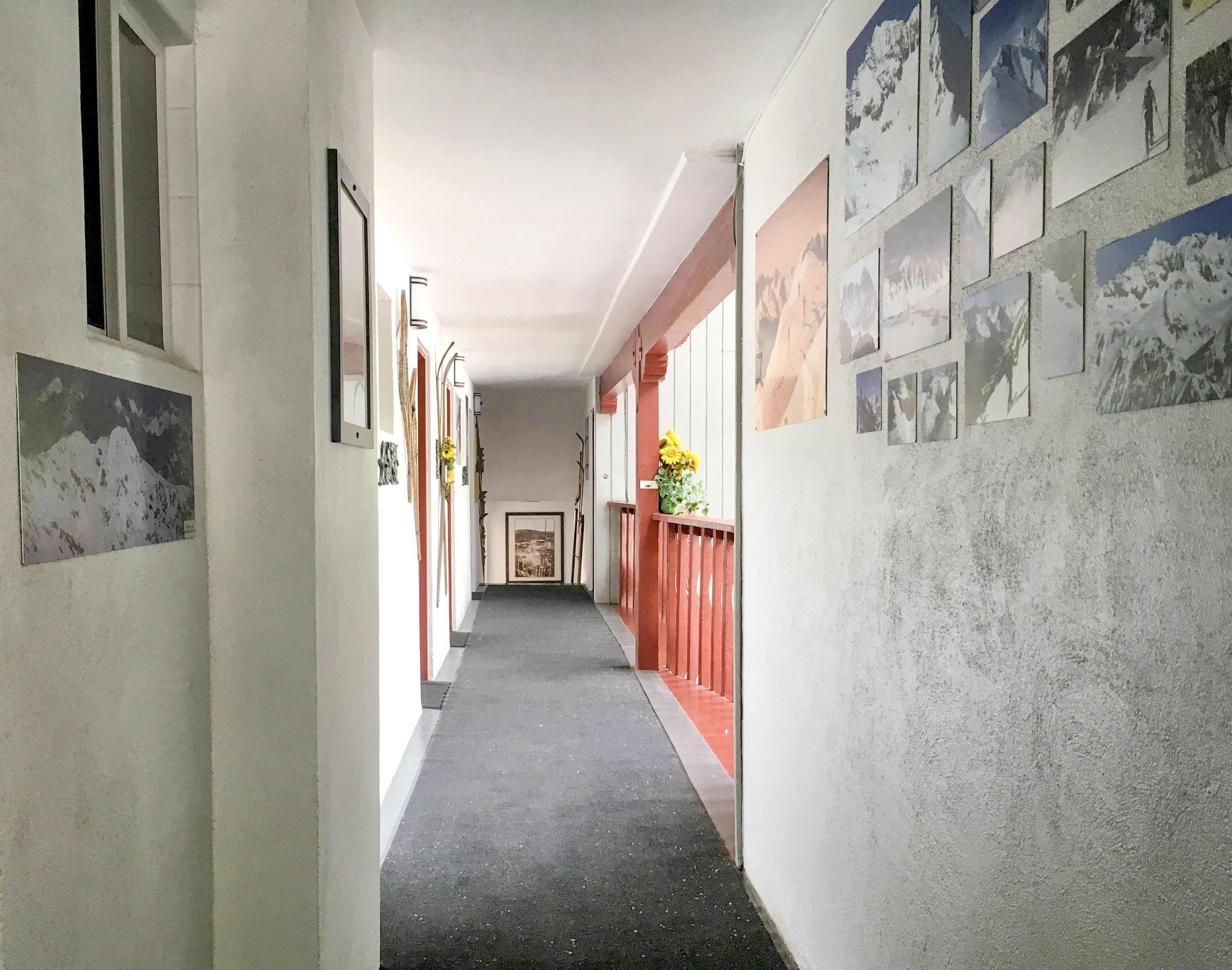 A corridor with framed pictures on the walls, a red railing, and a flower vase.