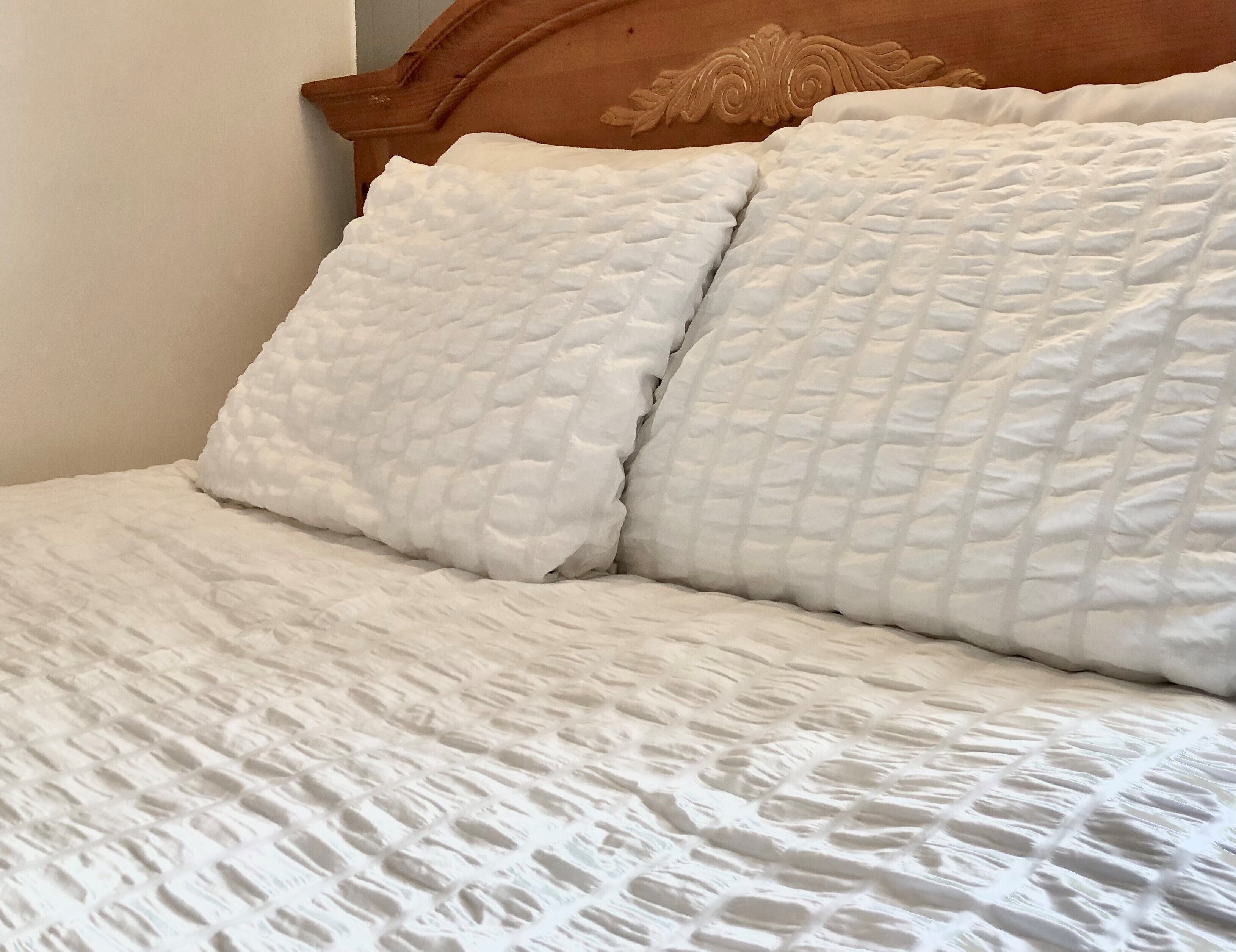 A bed with a quilted white bedspread and two pillows.