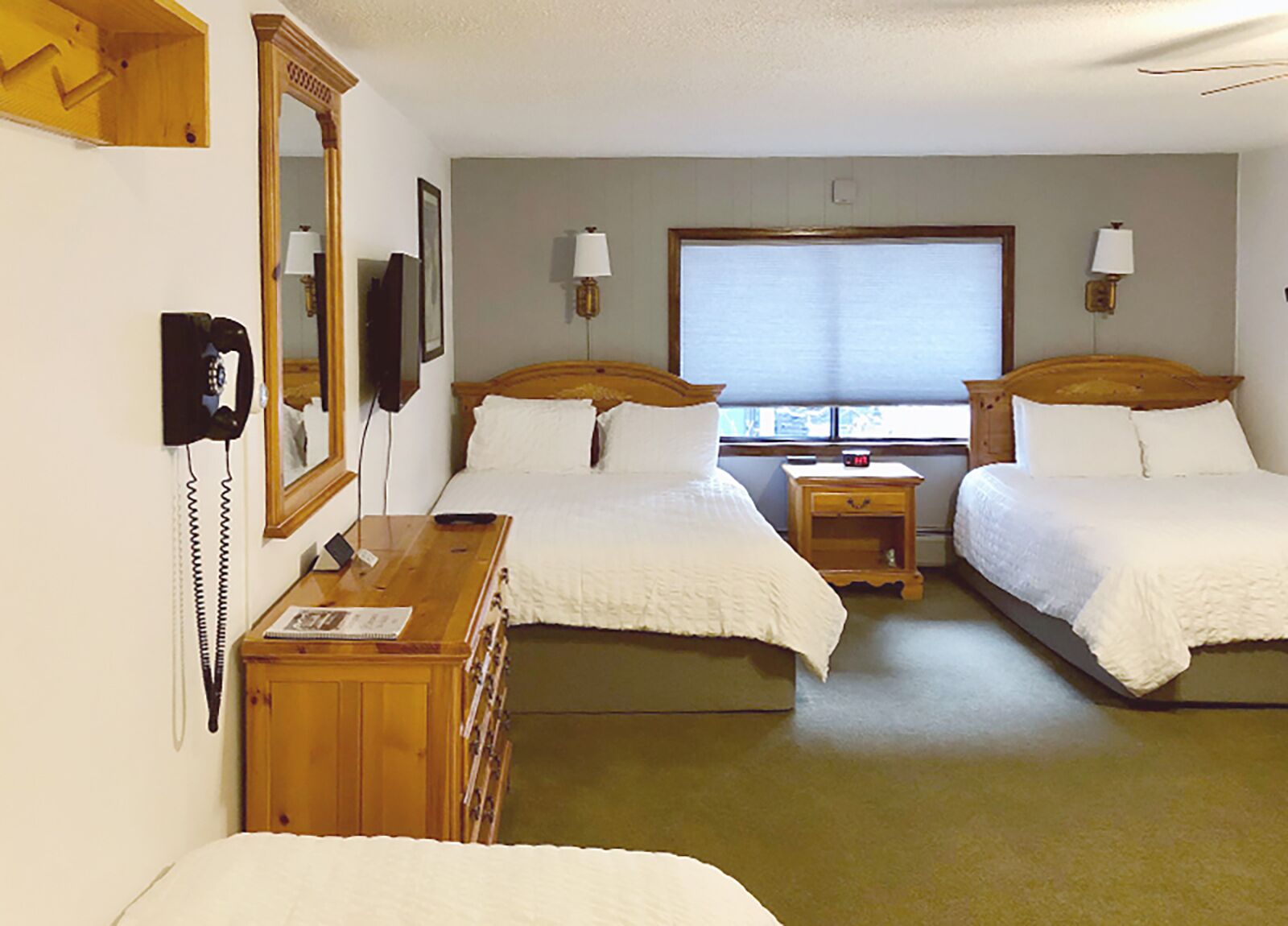 A hotel room with two single beds, a wooden dresser, a telephone, and a window with blinds.