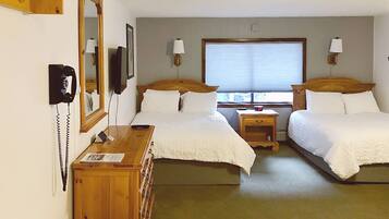 A hotel room with two single beds, a wooden dresser, a telephone, and a window with blinds.
