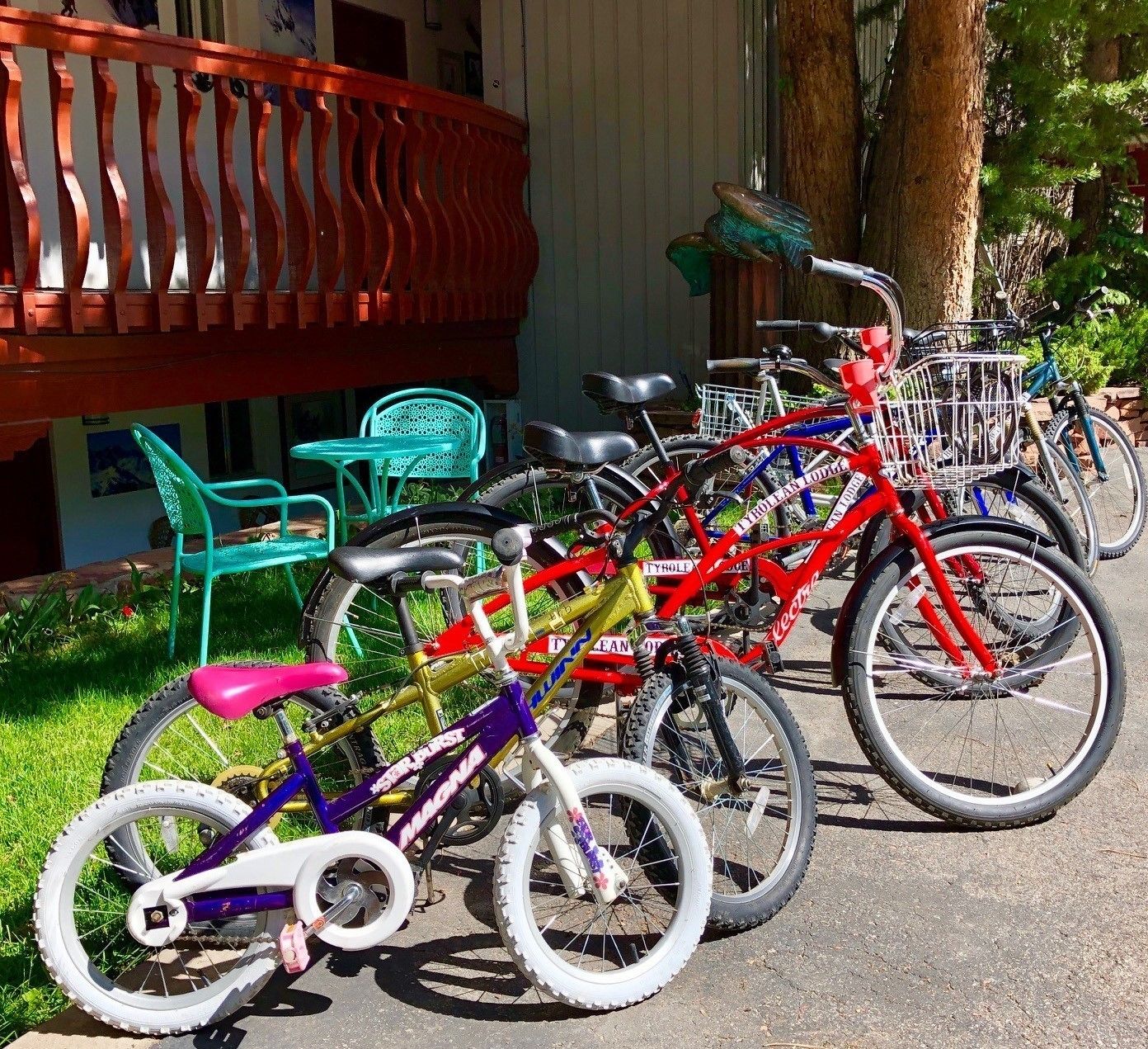 A row of bicycles parked outside a building with a red railing and a green chair nearby.