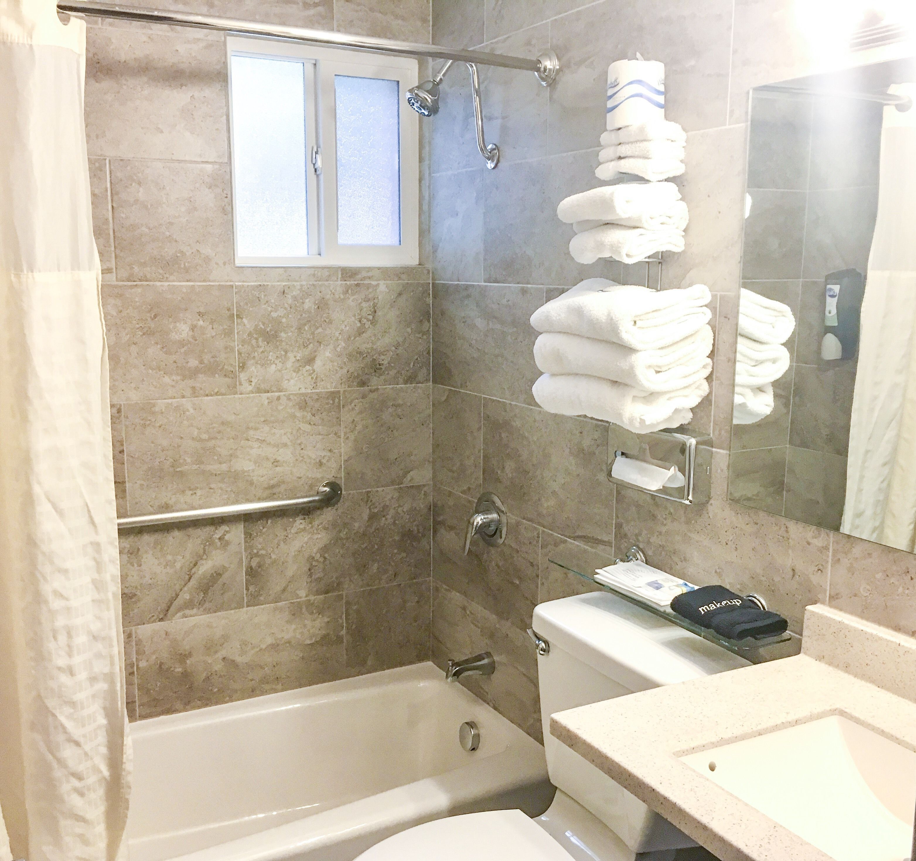 Un baño con bañera, inodoro y repisas de vidrio con artículos de aseo.