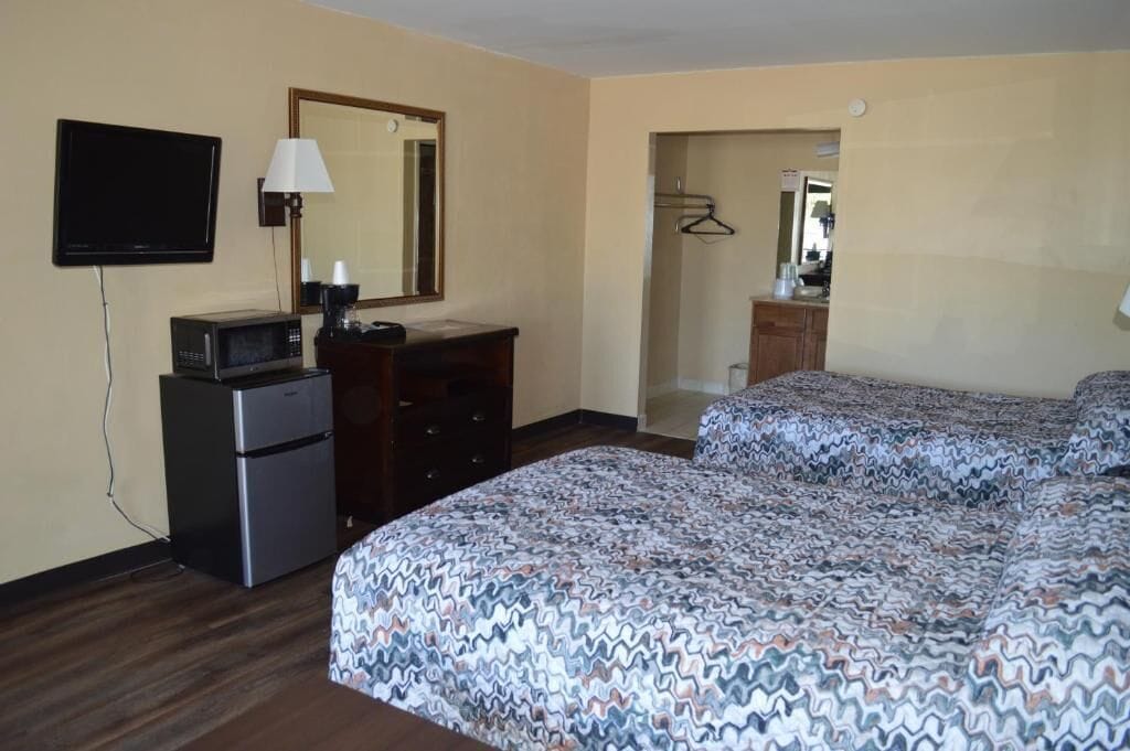 A hotel room with a bed, a desk with a microwave, a TV, a mirror, and a walk-in closet.