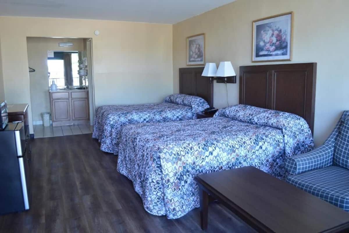 A hotel room with two beds, a desk, a chair, a lamp, and a painting on the wall.