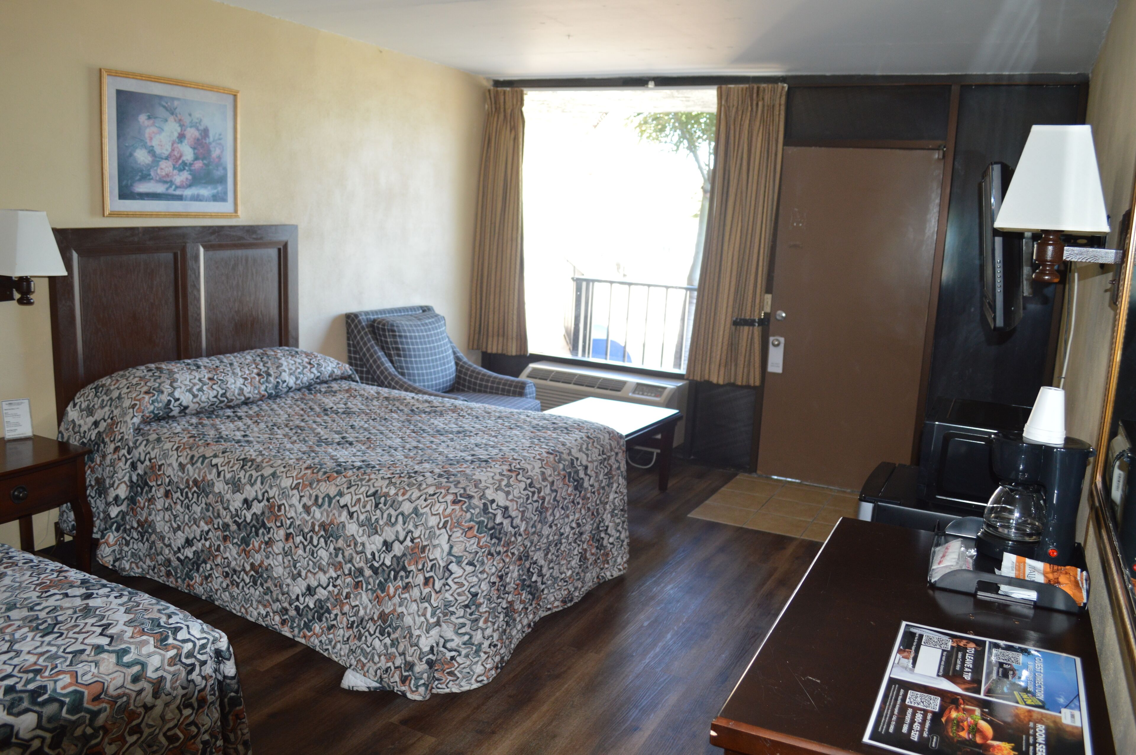 A hotel room with a bed, a chair, a desk, a coffee machine, and a window with curtains.