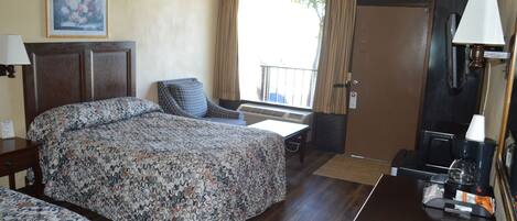 A hotel room with a bed, a chair, a desk, a coffee machine, and a window with curtains.