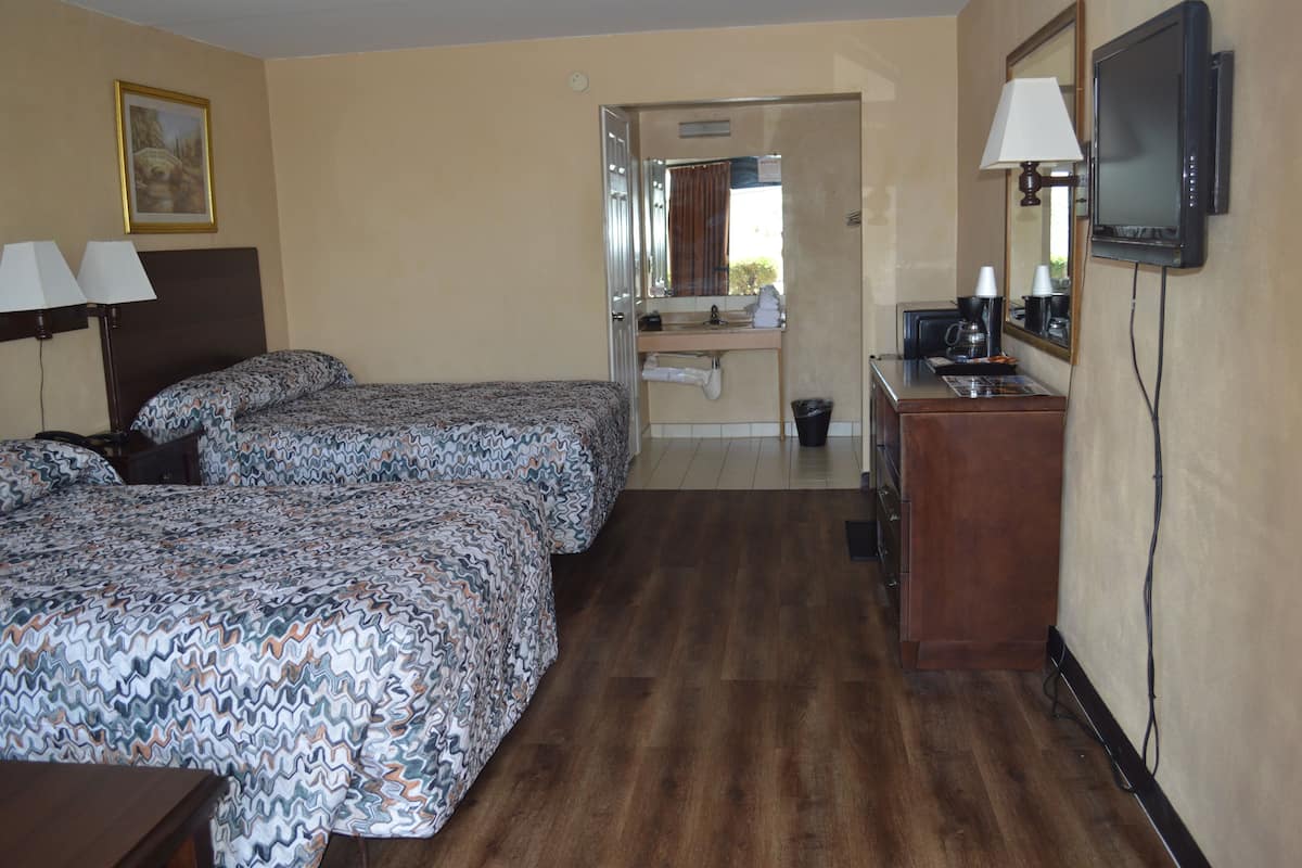 A hotel room with two beds, a desk with a lamp, a TV, and a bathroom visible through an open door.