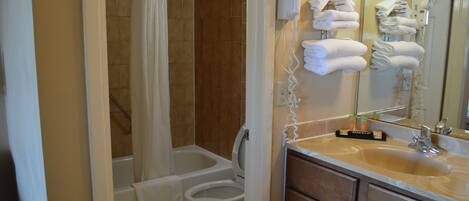 A bathroom with a bathtub, toilet, and sink. There are towels hanging on a rack and a hairdryer on the wall.