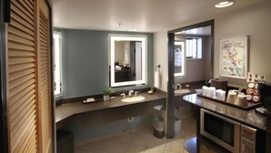 A modern bathroom with a vanity, sink, and mirror. There is a trash can and a microwave on the counter. - Adelaide Inn (Paso Robles)