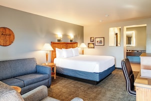 Habitación de hotel con cama, sofá, escritorio y baño visible a través de una puerta abierta.