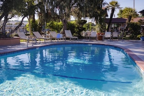 A clear swimming pool with lounge chairs and a tiled deck.