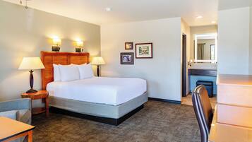 A hotel room with a bed, bedside lamps, a desk, a chair, a mirror, and framed pictures on the wall.