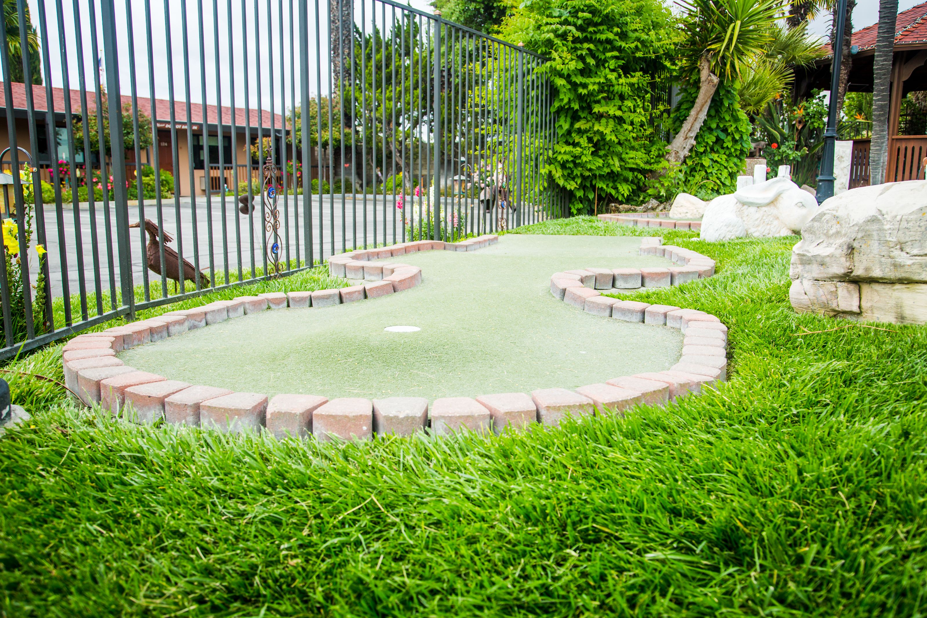 A miniature golf course with a green putting surface, surrounded by a brick border and lush green grass.